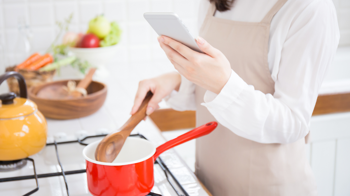 Decorative image of woman cooking at an oven with her phone in her hand